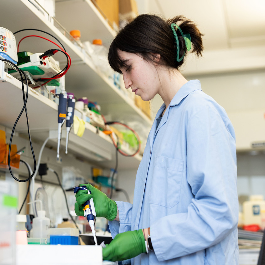 Student with a lab instrument wearing a blue lab coat